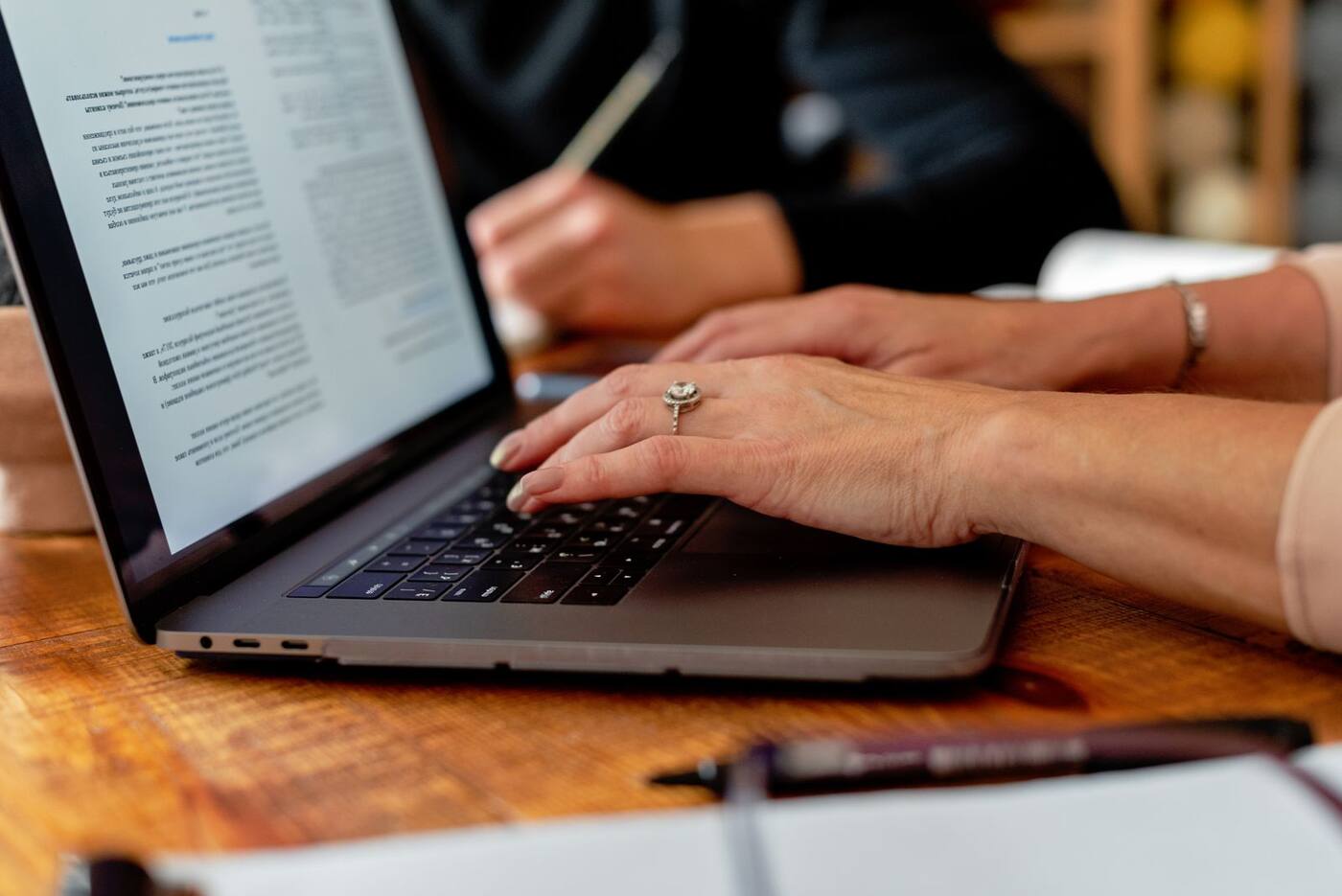 Manos escribiendo en una notebook apoyada en una mesa de madera